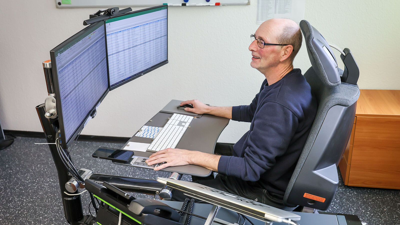 Schmerzfrei Arbeiten im Liegen Carsten Schönebeck an seiner Arbeitsstation mit zwei großen Monitoren, magnetischem Pult für Tastatur, Handy und Mousepad – hier im Sitzen.