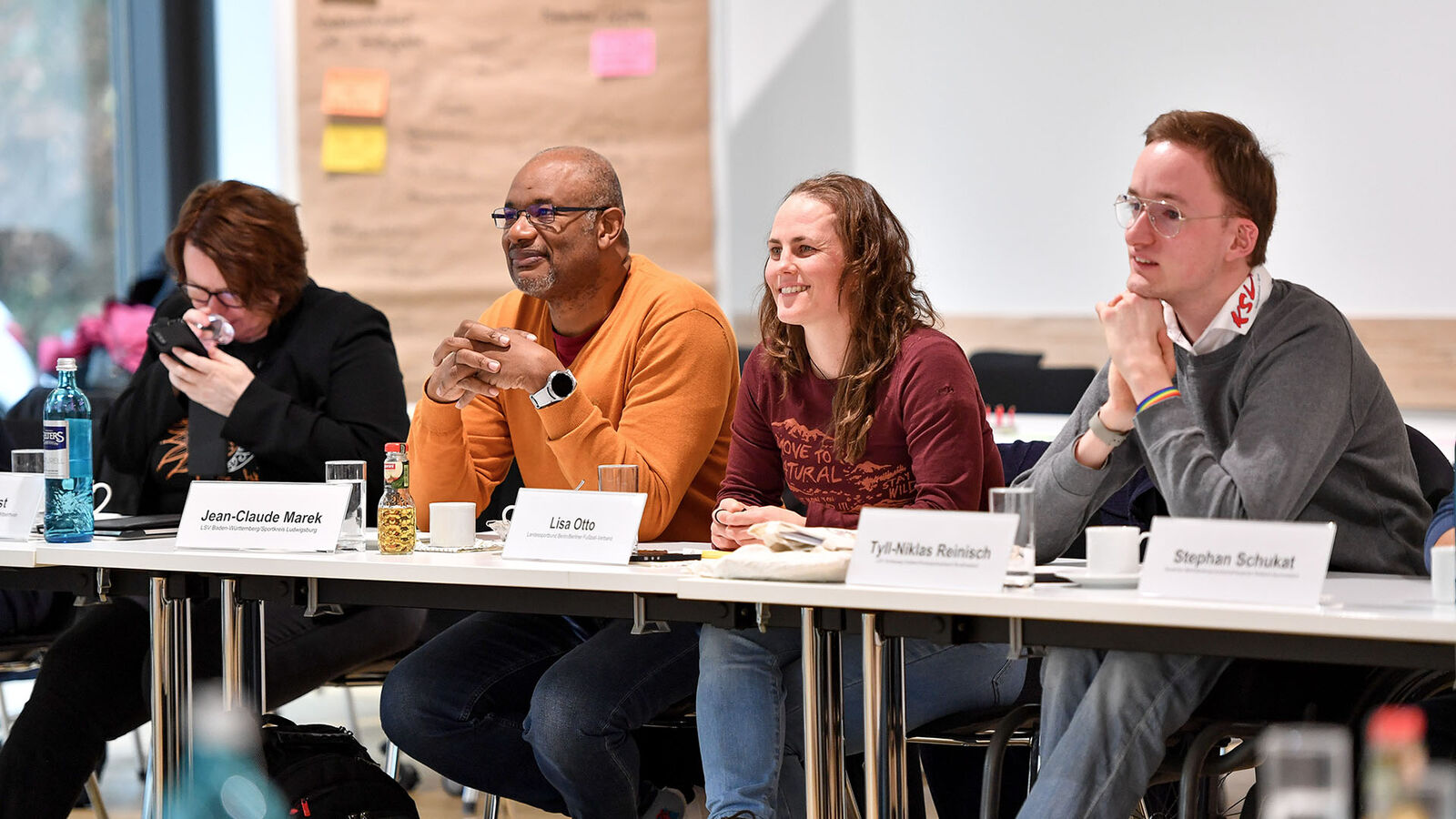 Vier Event-Inklusionsmanager sitzen in einer Reihe an einem Tisch, Namensschilder stehen vor ihnen. 