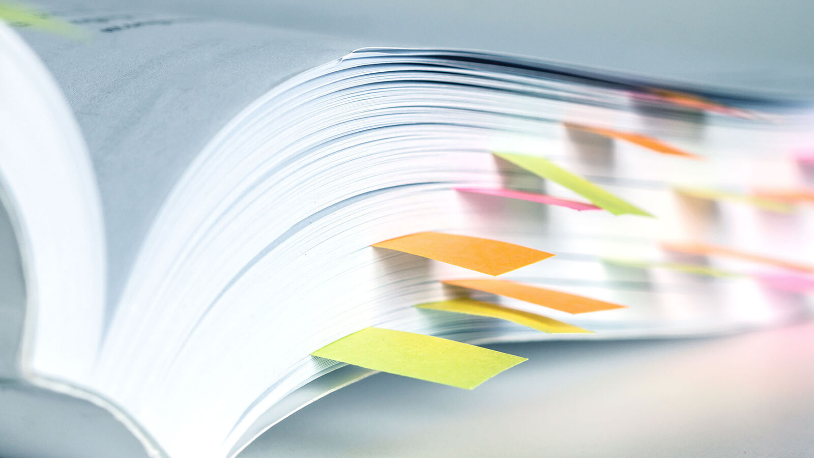 Symbolbild: Ein aufgeschlagenes Buch, auf vielen Seiten sind bunte Post-it-Zettel als Lesezeichen eingeklebt.