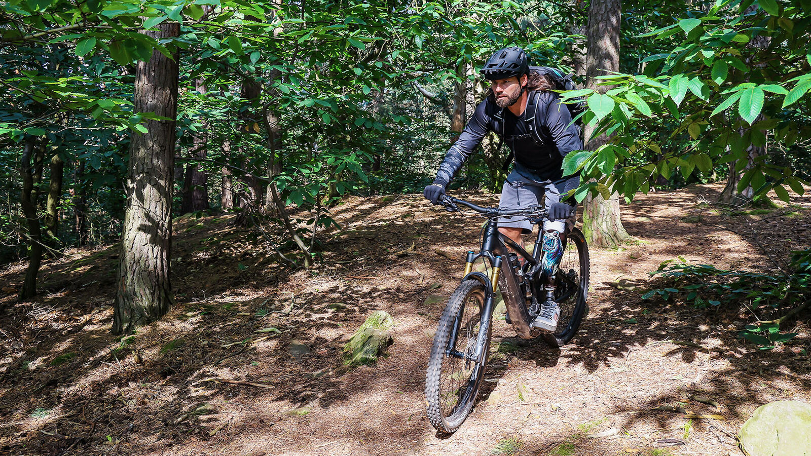Alexander Butz beim Downhill-Biken Alexander Butz fährt mit einem dunklen Mountainbike einen steilen Waldweg hinunter. Es ist ein sonniger Tag.