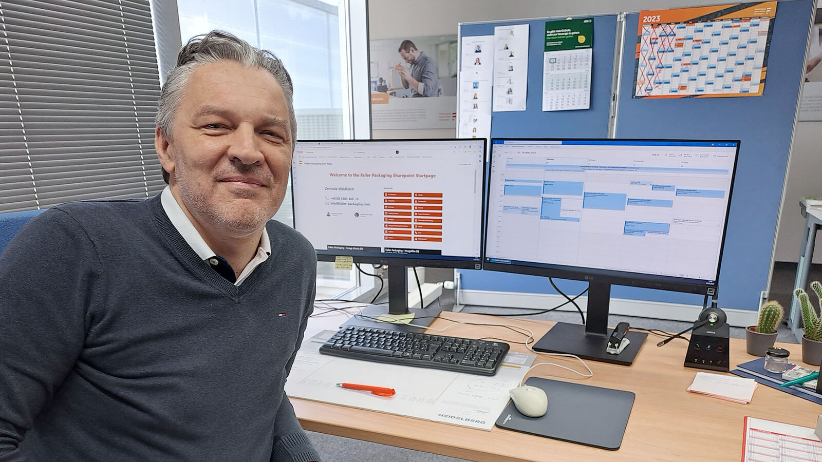 Dieter Hager sitzt an seinem Schreibtisch. Er ist zur Kamera gedreht, der Blick fällt auf ihn und die Displays von zwei großen Monitoren.