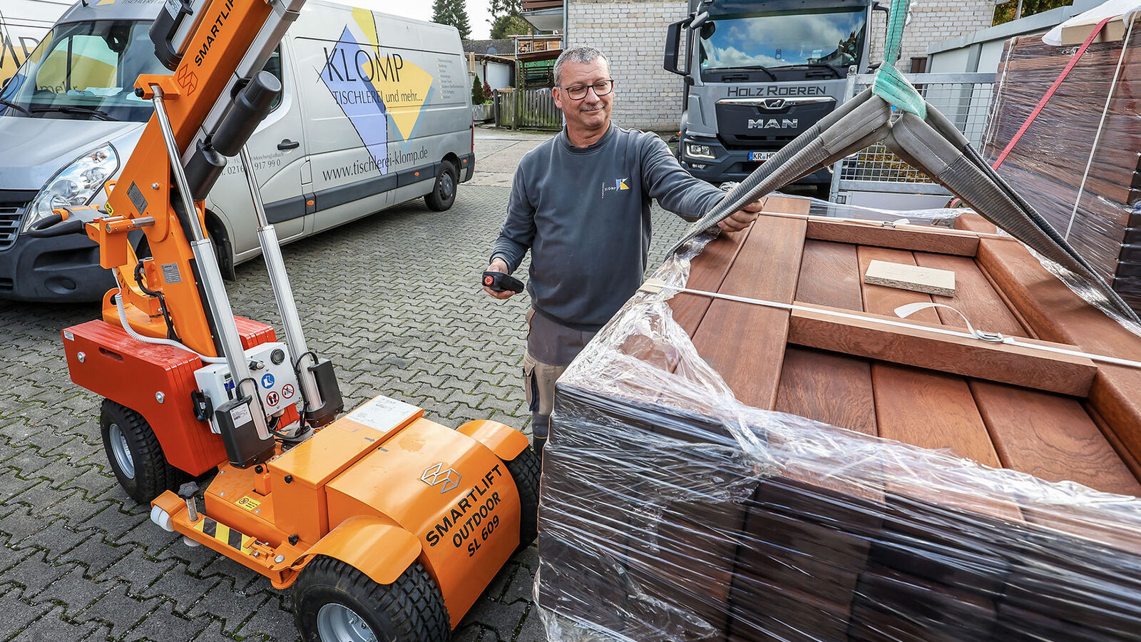 Stefan Baches steht vor einem Holzstapel, der Glasroboter steht nehmen ihm.