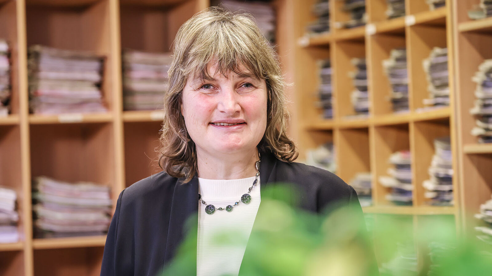 Porträt von Dr. Petra Bungert. Die Richterin steht in einem mit hohen Regalfächern ausgekleideten Raum. In den Fächern liegen zahllose Akten.