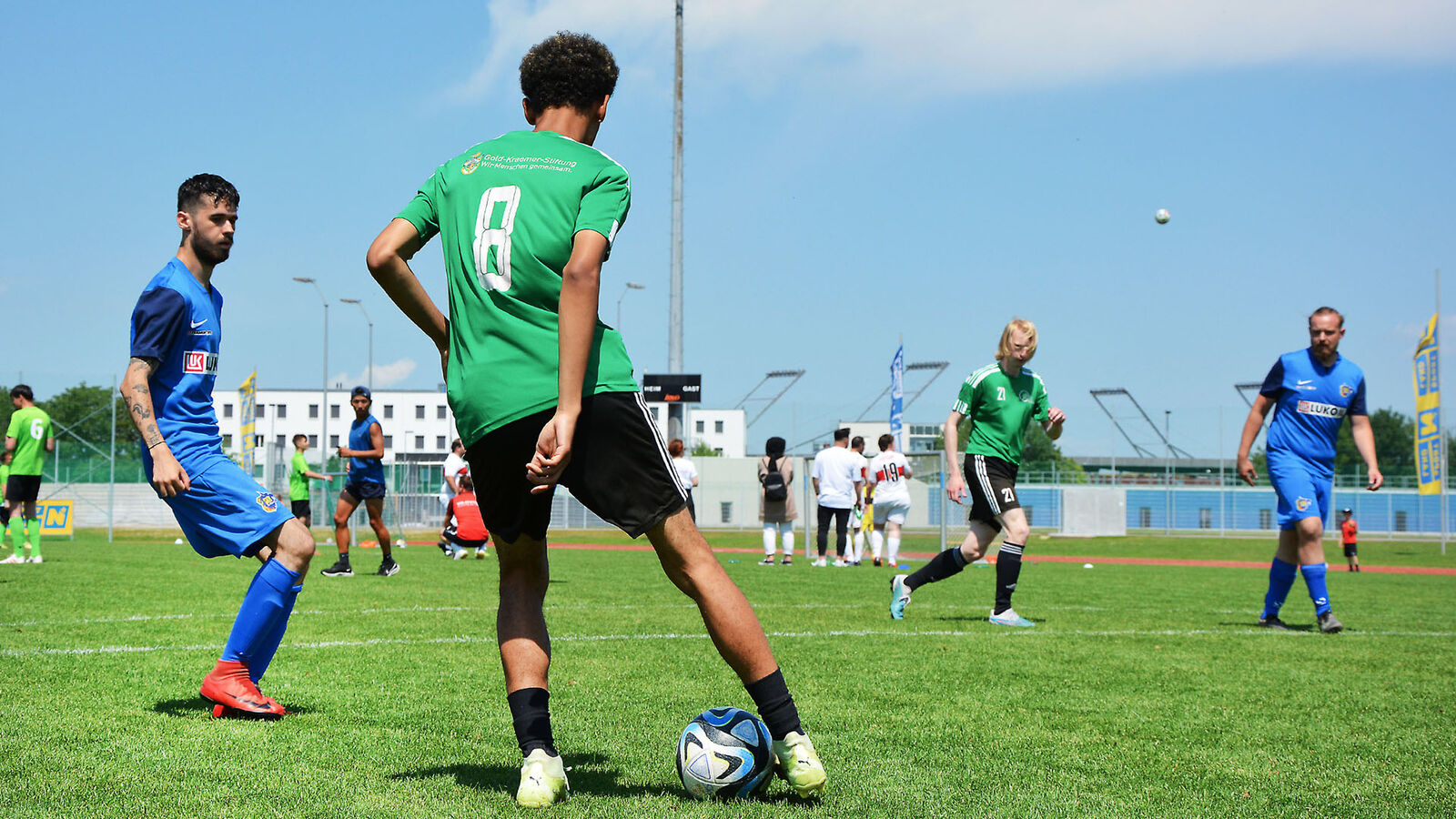 Behinderung im Sport Das Foto zeigt eine Trainingsszene auf einem Fußballplatz. Die Spieler tragen grüne und blaue Trikots.