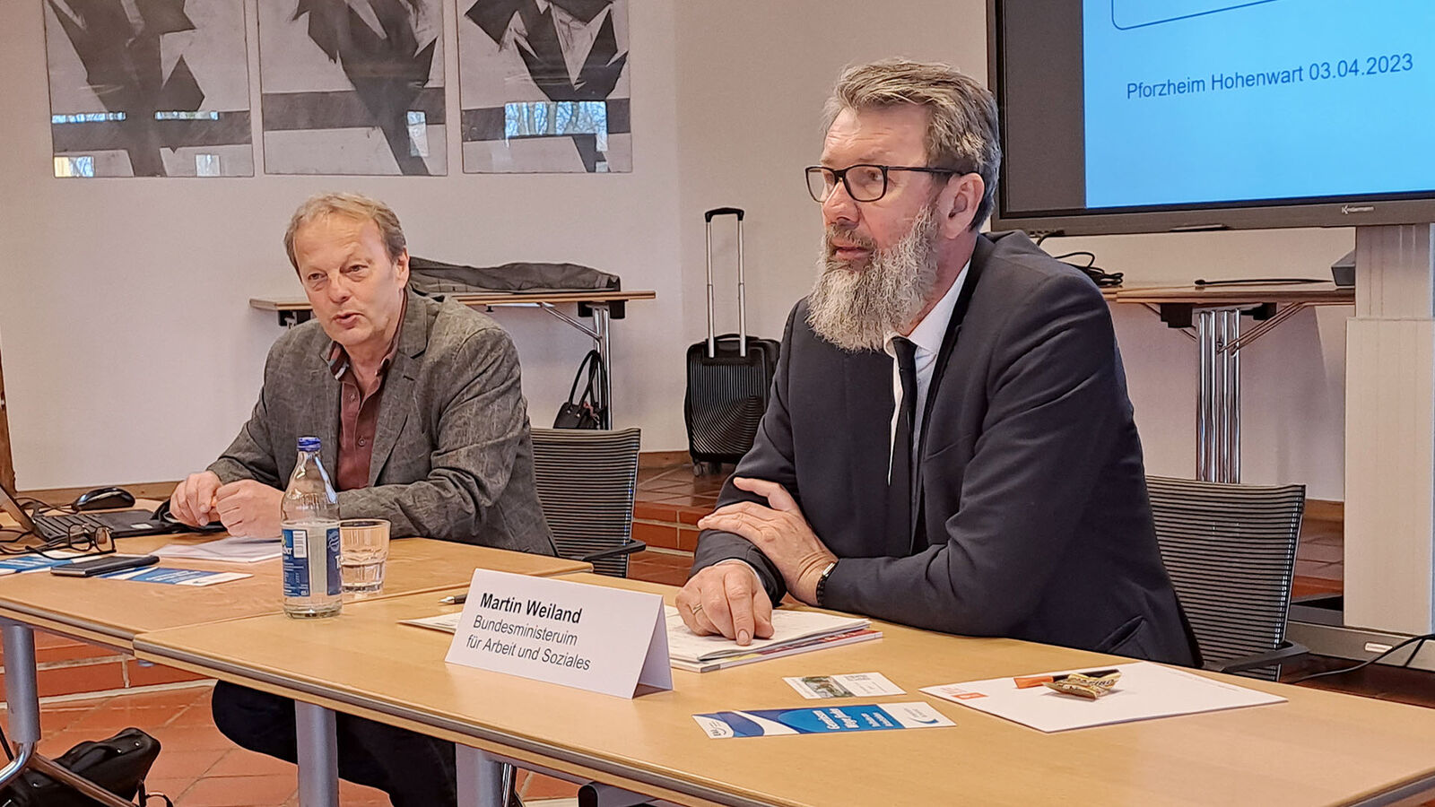 Guido Kleb und Martin Weiland (rechts im Bild) sitzen vor Publikum an einem langen Tisch.