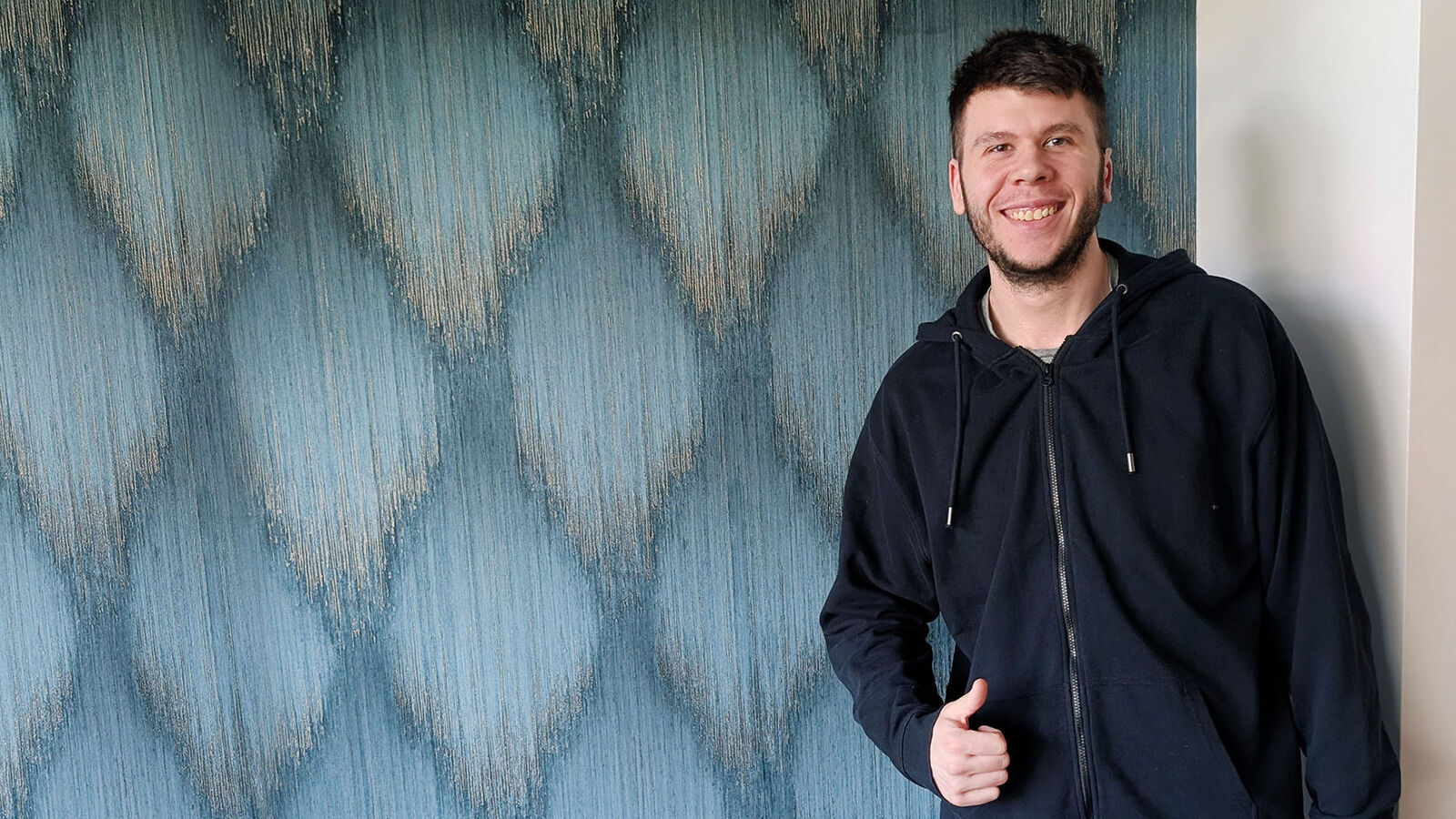 Jean-Michel Hess steht vor einer Wand mit blaugemusterter Tapete.