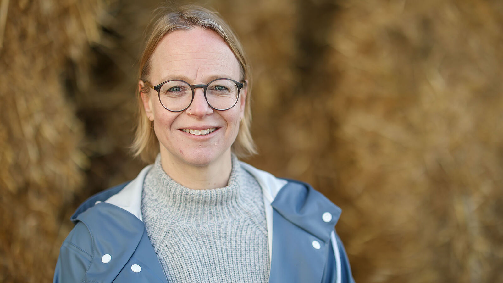 Eileen Düchting steht in einem Winterpullover und blauer Regenjacke vor zwei großen Heuballen.