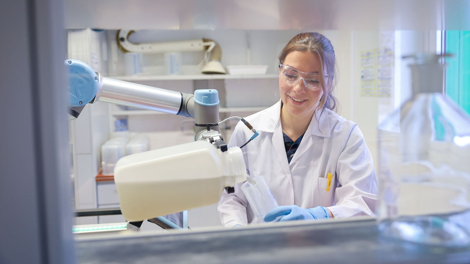 Mitarbeiterin am Cobot Eine Mitarbeiterin arbeitet mit dem Cobot zusammen - es wird Schlamm ausgegossen.