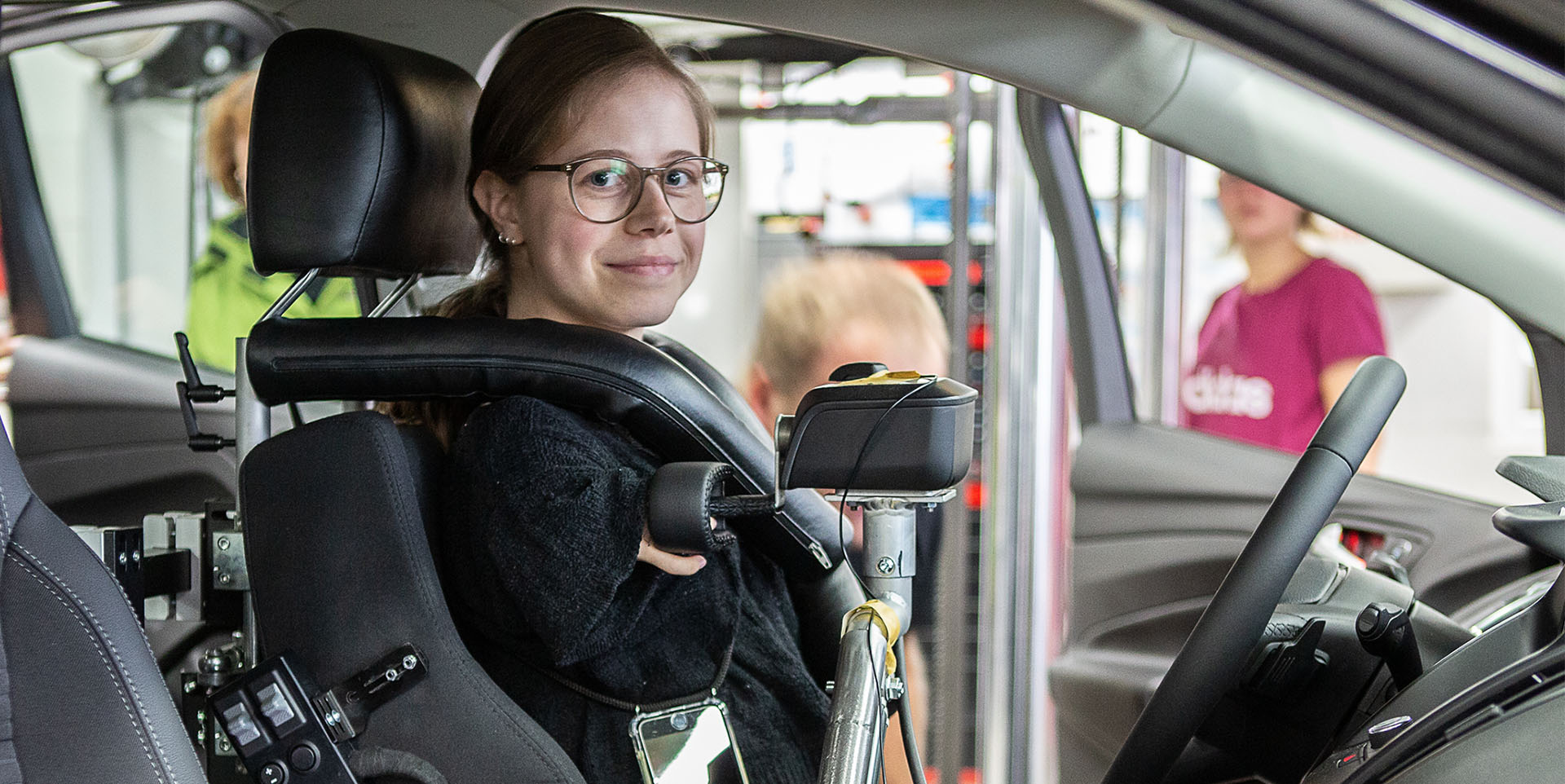 Eine Frau mit verkürzten Armen sitzt in einem speziell umgebauten Pkw mit nach oben gelegter Schaltvorrichtung. Die Fahrerin kann diese mit zwei Fingern bedienen. 