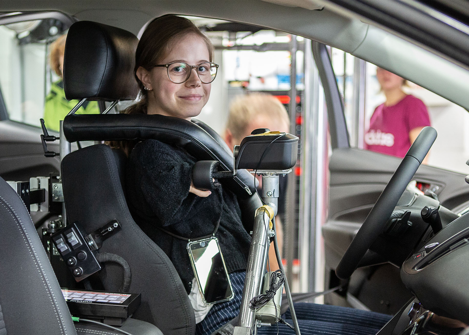 Eine Frau mit verkürzten Armen sitzt in einem speziell umgebauten Pkw mit nach oben gelegter Schaltvorrichtung. Die Fahrerin kann diese mit zwei Fingern bedienen. 
