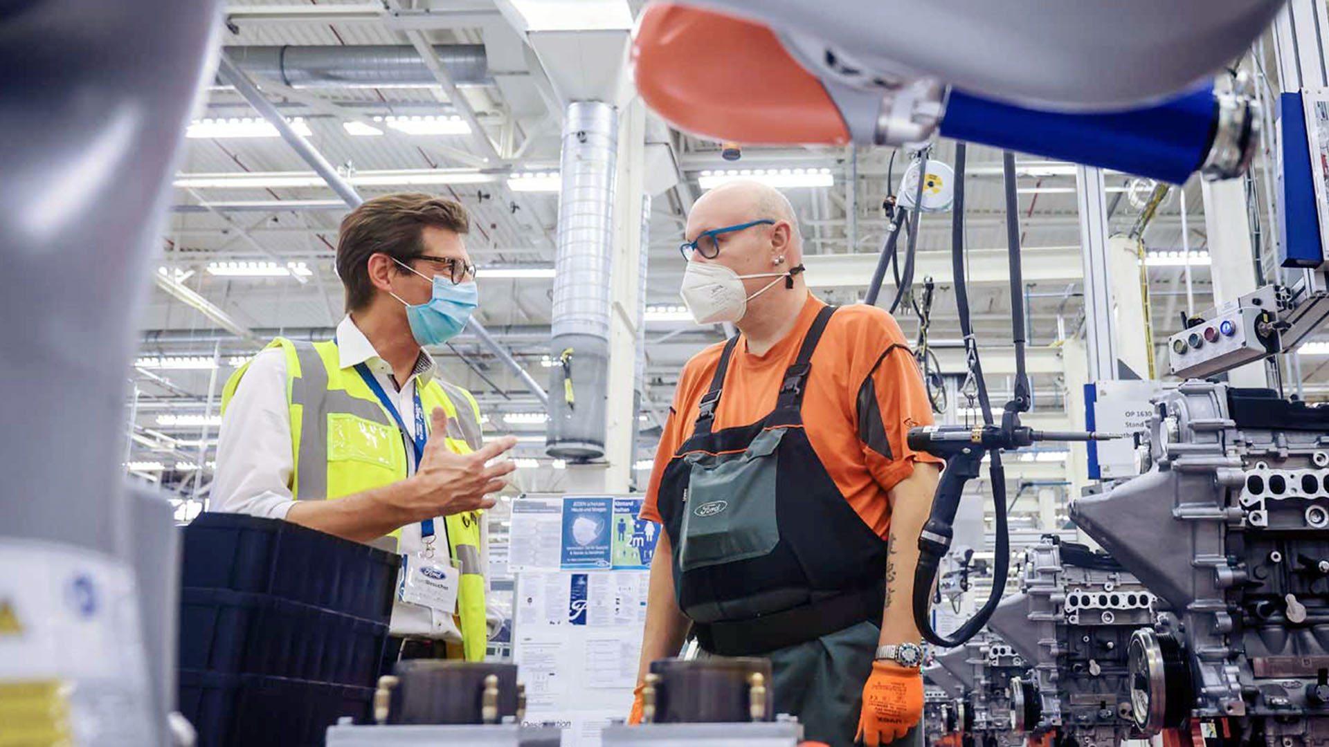 Zwei Männer stehen am Arbeitsplatz mit dem Kobot und unterhalten sich.