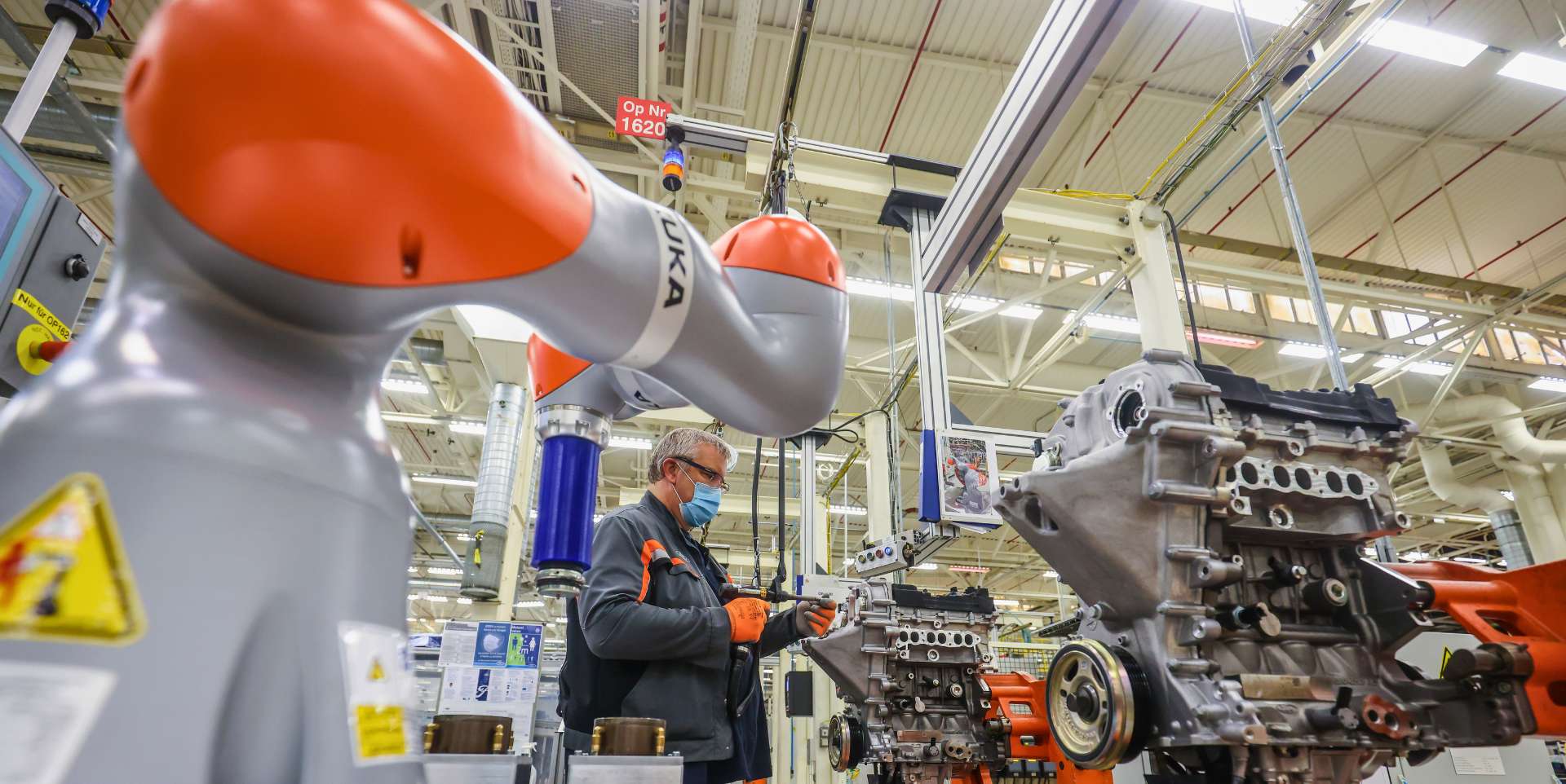 Kollege Robotoer Ein kompakter Roboter mit rundlichen Formen arbeitet direkt neben einem älteren Mann am Fließband.