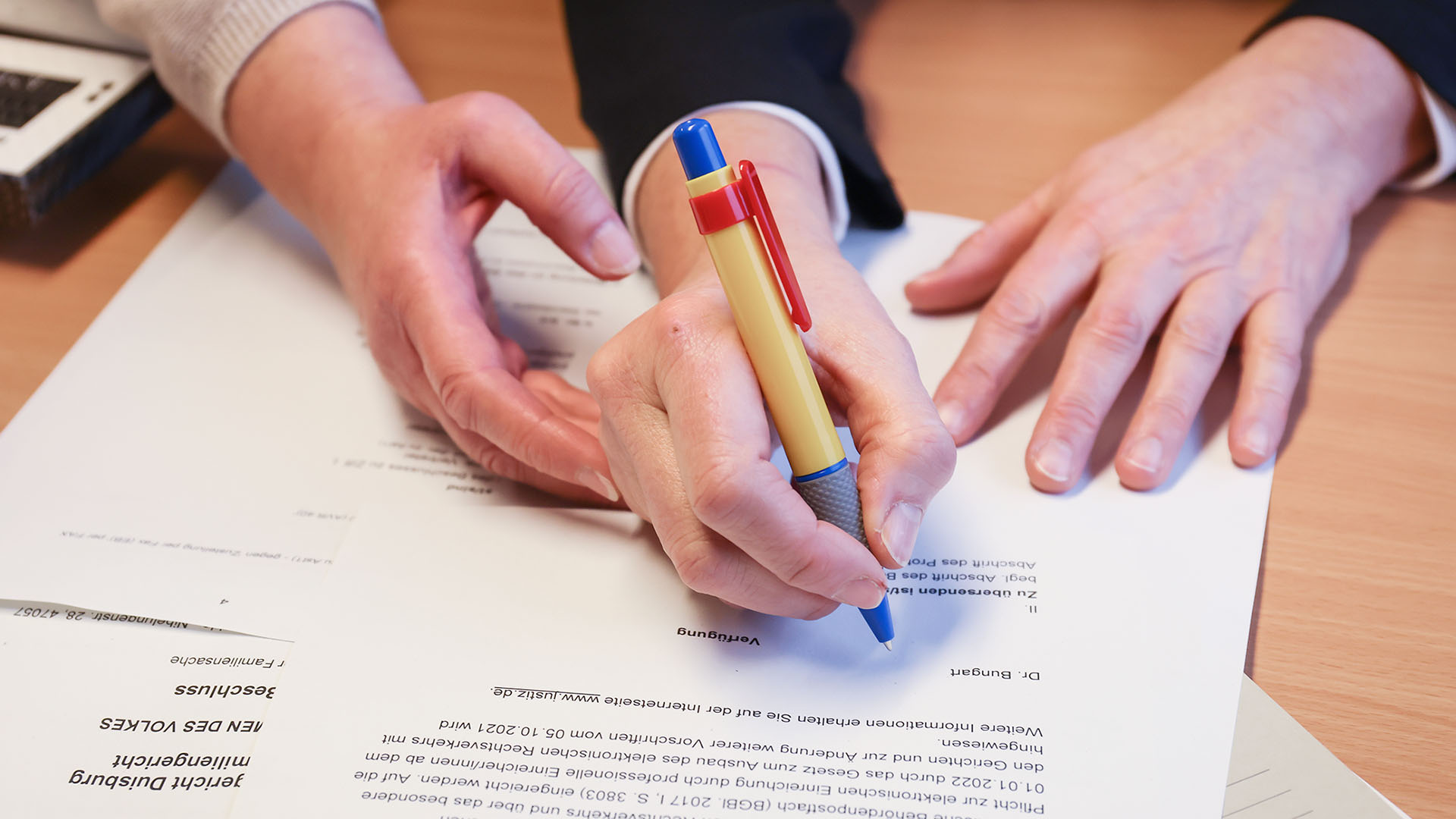 Das Foto zeigt die beiden Hände einer Frau mit einem schwarzen Jacket. Über einem Brief mit dem Schriftzug "Dr. Bungert" hält die rechte Hand einen bunten Kugelschreiber. Diese Hand wird von einer anderen Frauenhand geführt.
