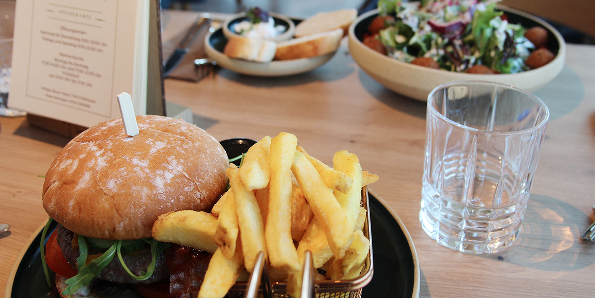 Gedeckter Bistrotisch mit einem Burger- und einem Falafel-Teller.