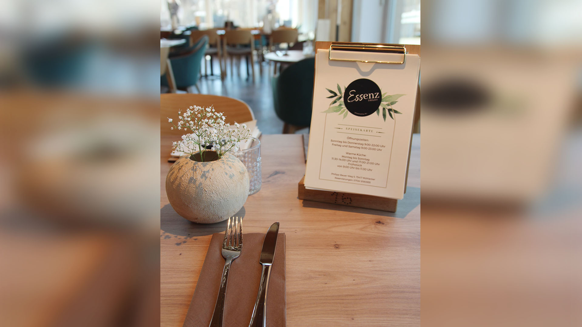 Ein Bistrotisch mit kleiner Speisekarte als Tischaufsteller und einer kugeligen Blumenvase mit Schleierkraut.