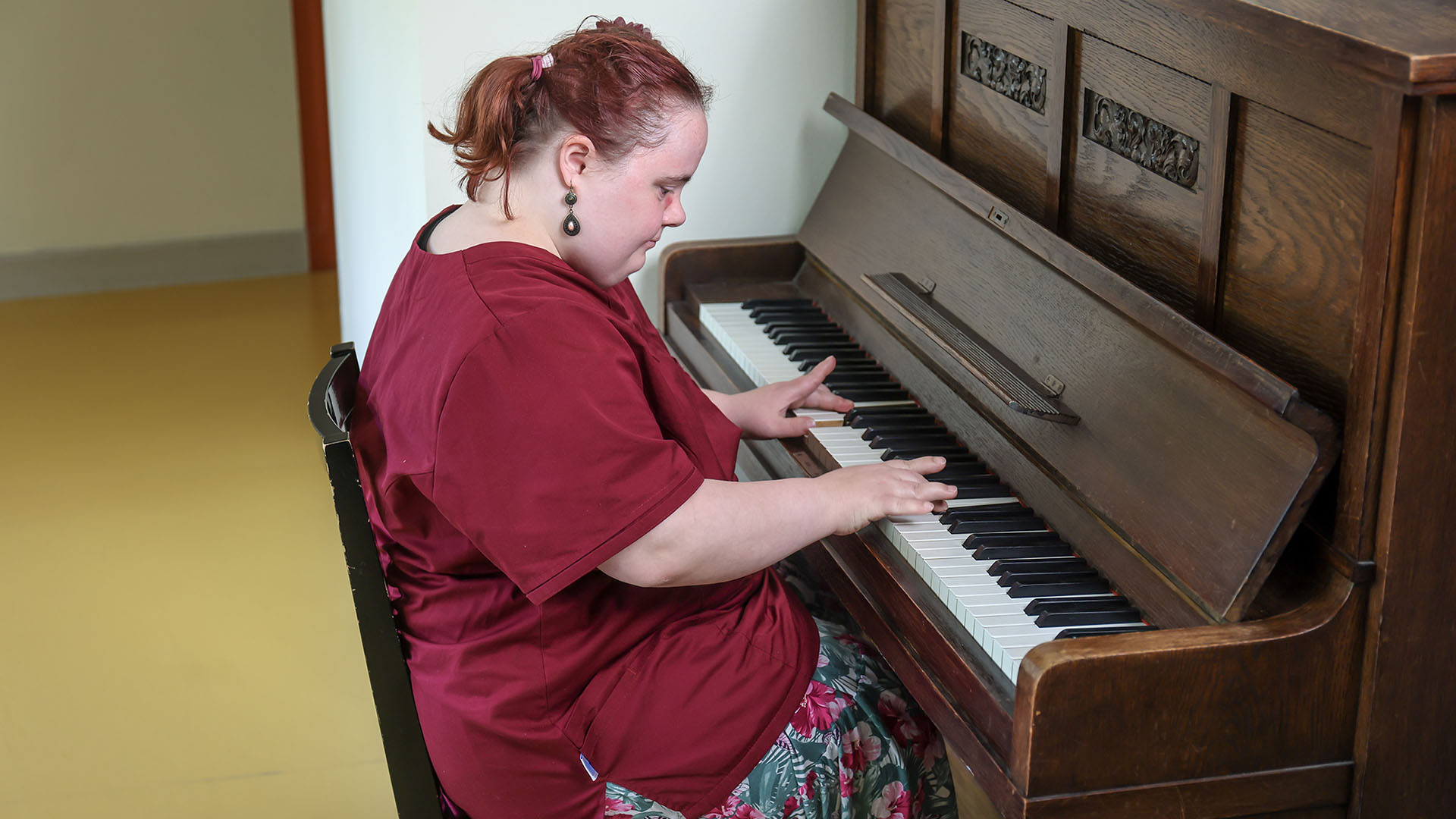 Franziska Wolf sitzt an einem alten Klavier aus dunklem Holz und spielt. Der Blick fällt von der Seite auf sie.