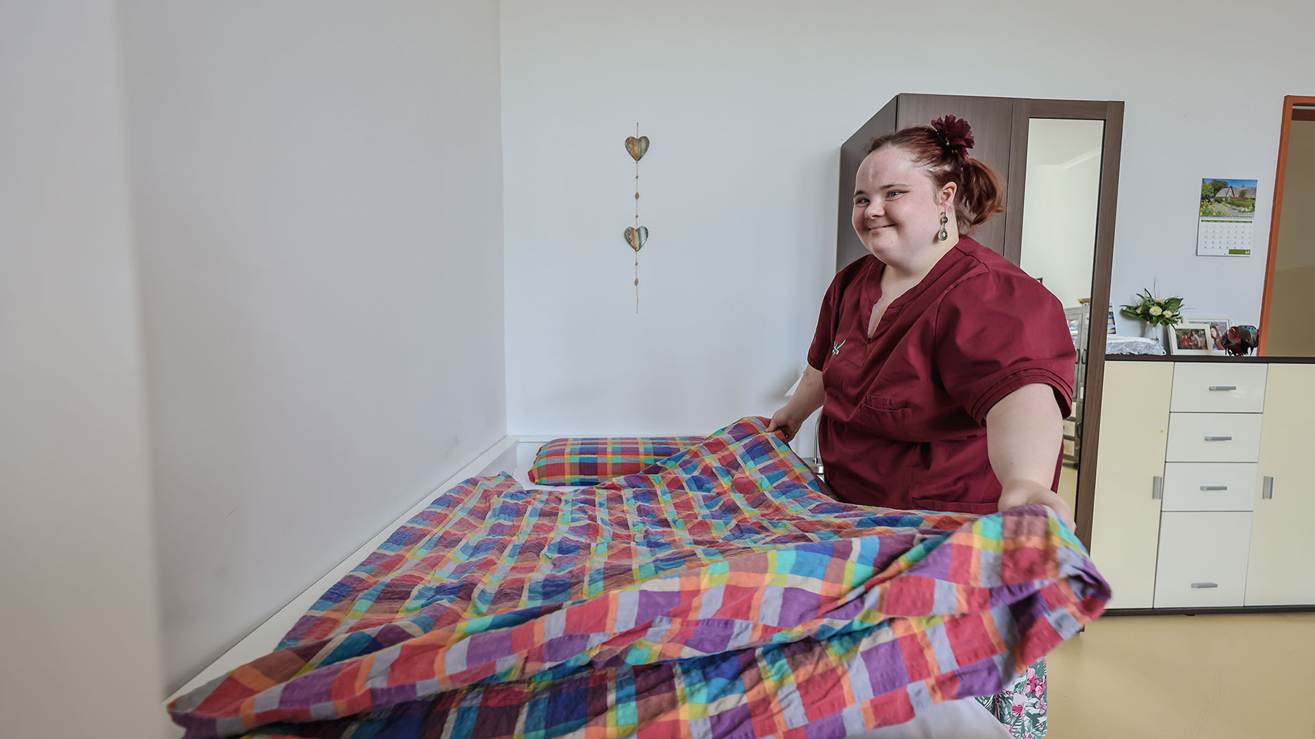 Franziska Wolf streicht ein buntkariertes Oberbett in einem der WG-Bewohnerzimmer glatt. Der Blick fällt seitlich auf sie.