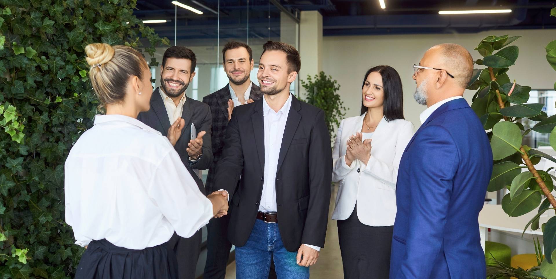 Eine Gruppe von Menschen steht im Eingangsbereich eines Unternehmens und begrüßt eine junge Frau.