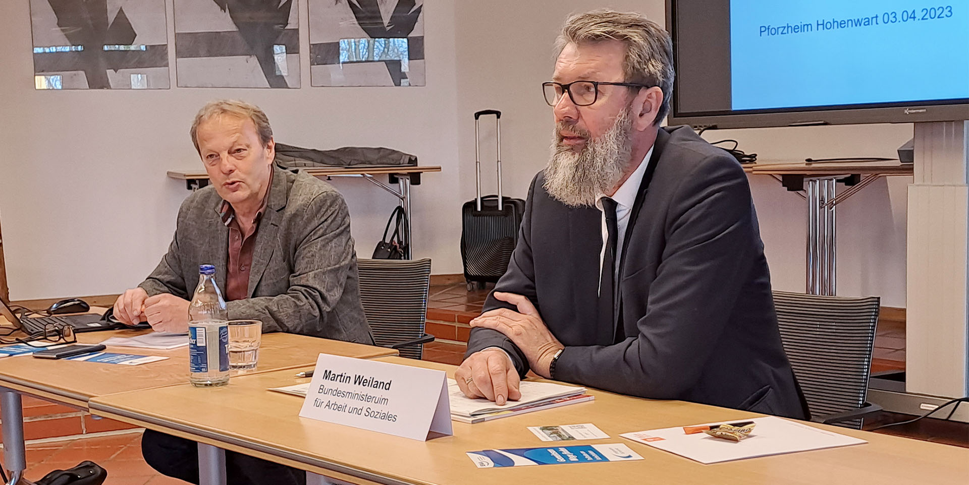 Guido Kleb und Martin Weiland (rechts im Bild) sitzen vor Publikum an einem langen Tisch.