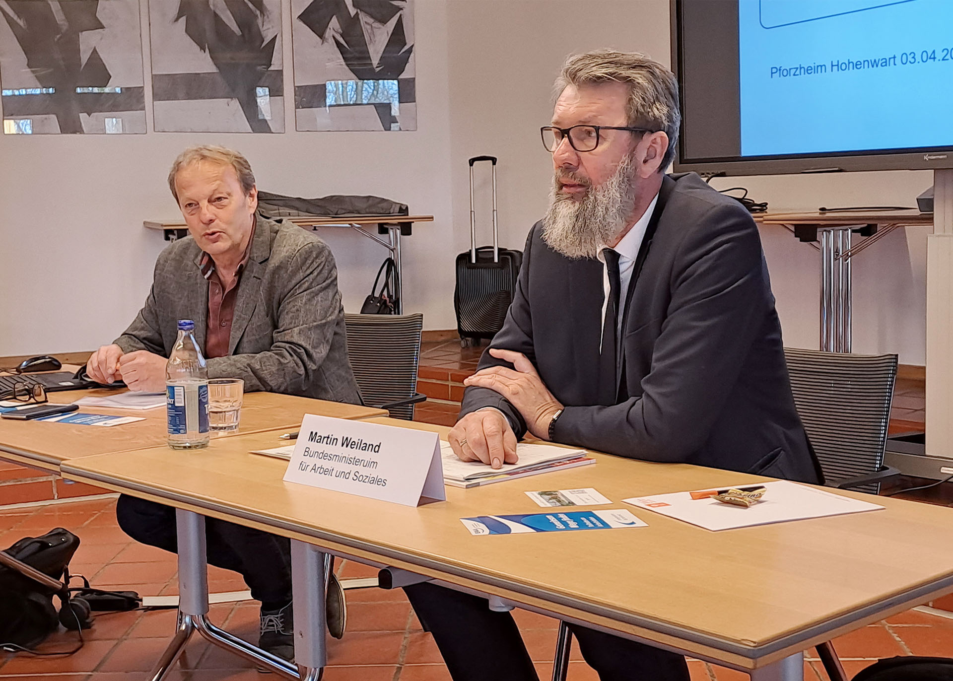 Guido Kleb und Martin Weiland (rechts im Bild) sitzen vor Publikum an einem langen Tisch.
