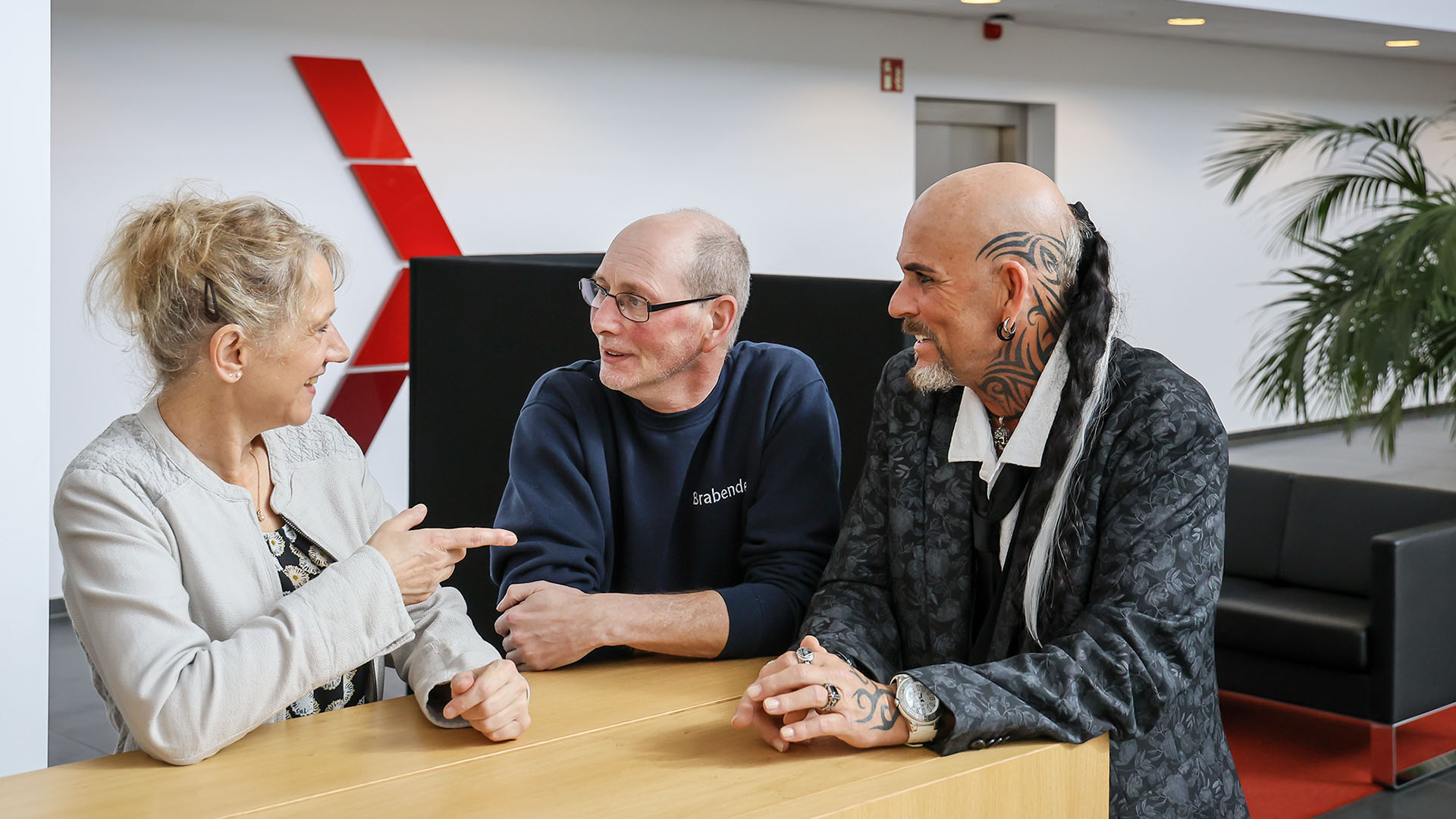 Sabine Stange, Carsten Schönebeck und Markus Sander (von li. n. re.) stehen in der Eingangshalle des Unternehmens Brabender und unterhalten sich. Im Hintergrund sind große Grünpflanzen zu sehen