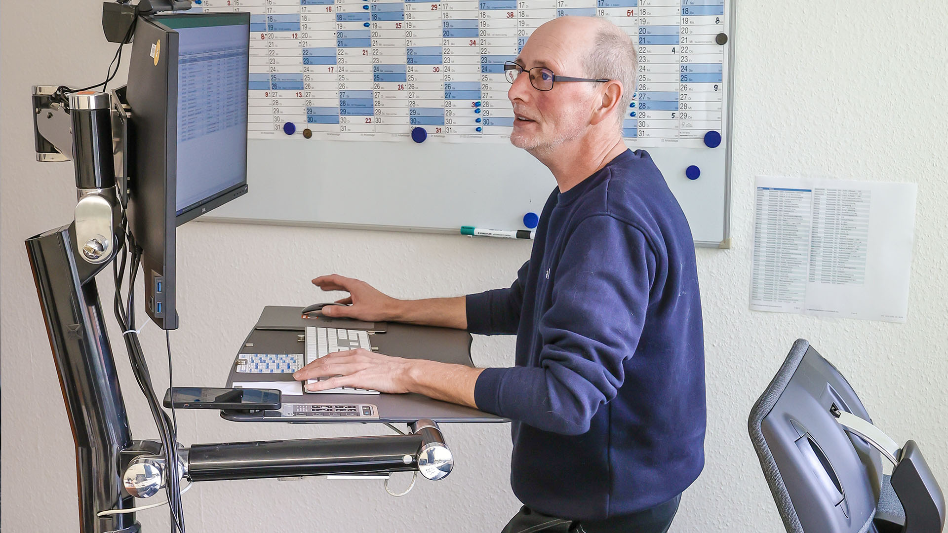 Carsten Schönebeck an seiner Arbeitsstation mit zwei großen Monitoren, magnetischem Pult für Tastatur, Handy und Mousepad – hier im Stehen.