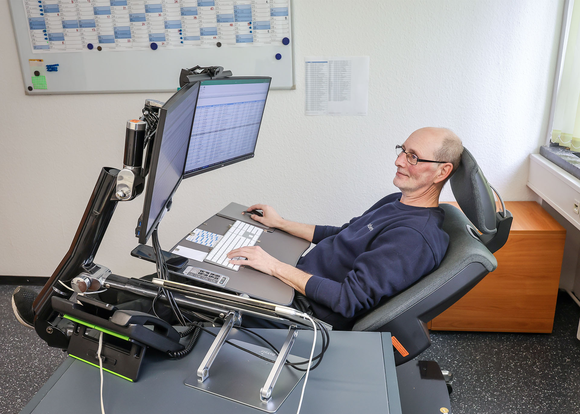 Carsten Schönebeck vor einem Spezial-Bildschirmarbeitsplatz mit Liegemöglichkeit.