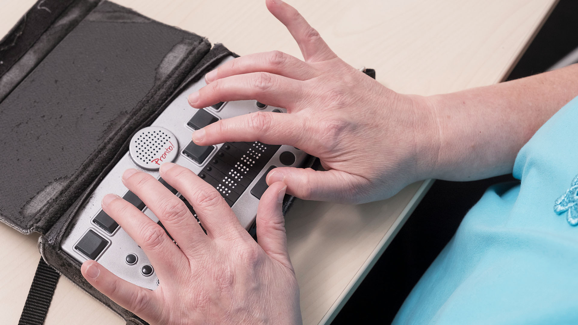 Das Foto zeigt ein kleines Gerät mit Brailletasten und Hände, die darauf tippen. Der Körper ist abgeschnitten.