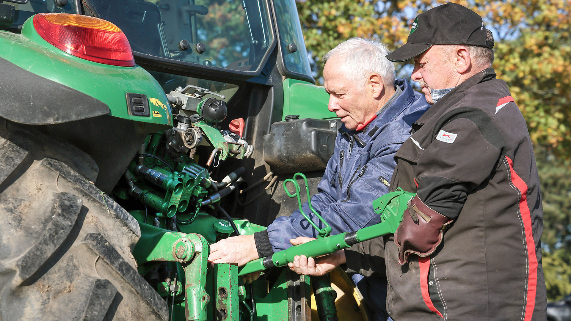 Wolfgang Leubner und seine Arbeitsassistenz stehen am Traktor und nehmen eine Einstellung vor.