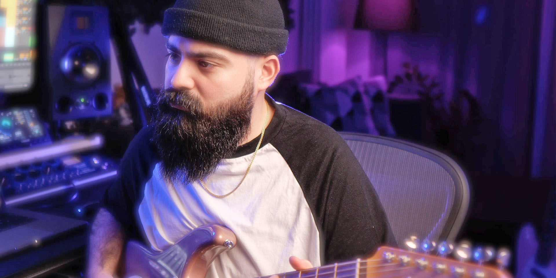 Cihan Ozaman sitzt mit Fischermütze und kurzärmeligem T-Shirt im Studio und spielt Gitarre