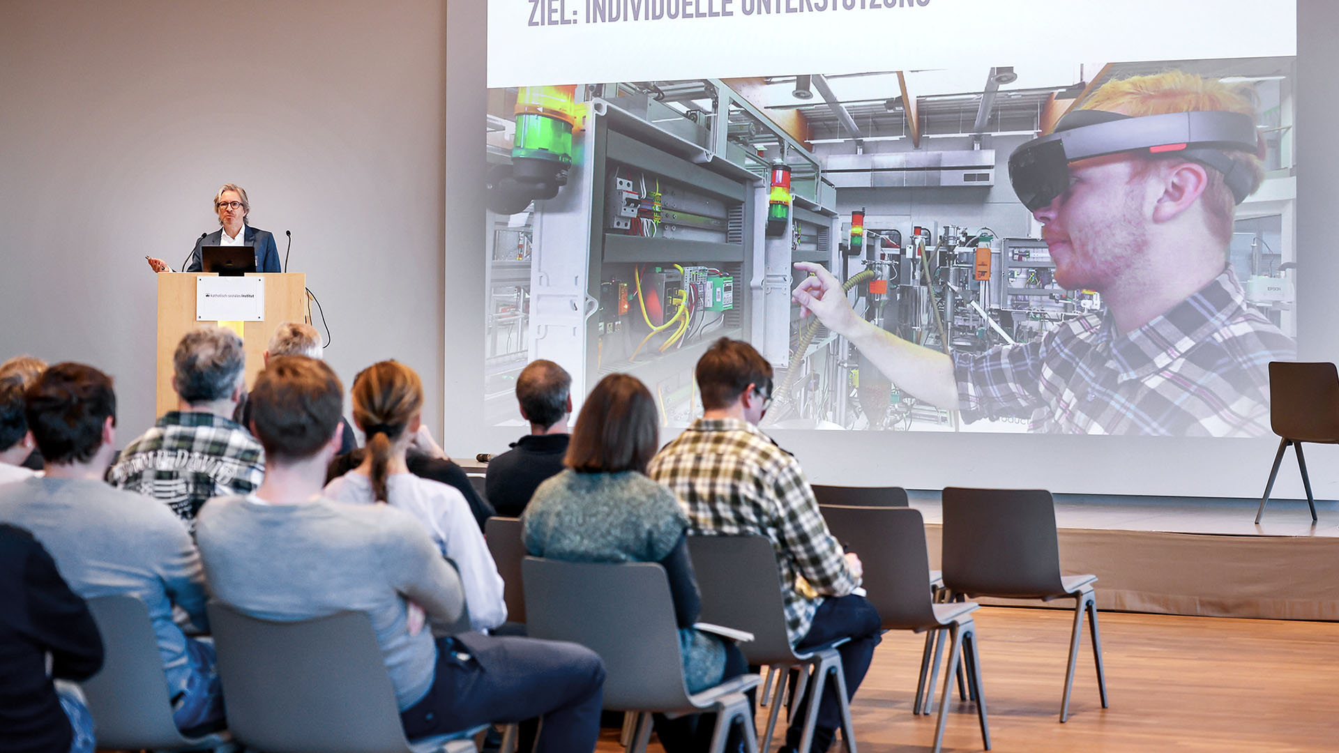 Ein Herr mittleren Alters, grauen Haaren und gepflegtem Drei-Tage-Bart steht an einem Rednerpult vor einem gut gefüllten Saal und hält einen technischen Vortrag.