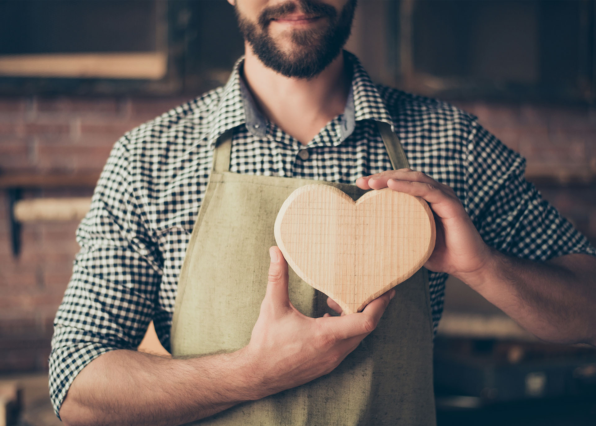 Ein Mann mit einer Schürze hält ein aus holz geschnitztes Herz in seinen Händen