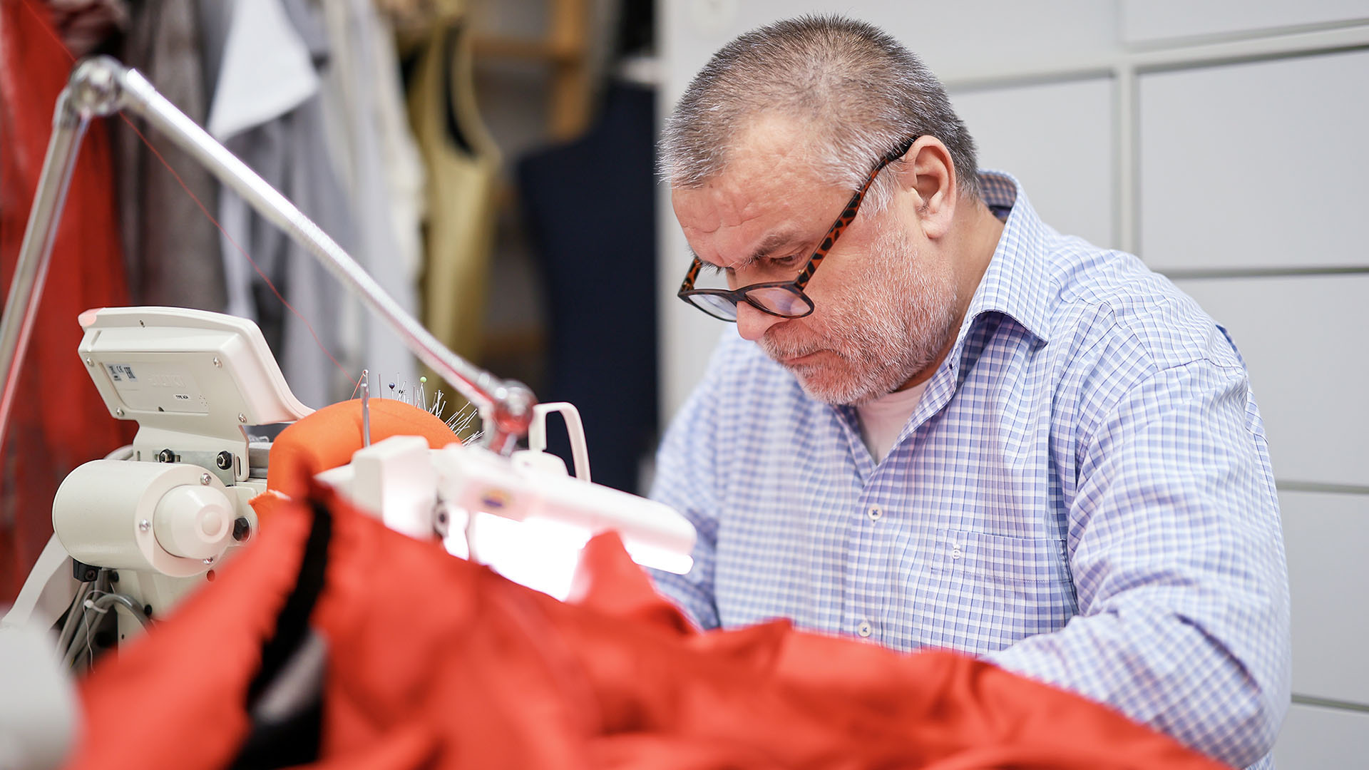 Der Herrenschneider Yusuf Aydoğan arbeitet hochkonzentriert an der Nähmaschine. Er ist dabei, einen weiten roten Umhang zu säumen.