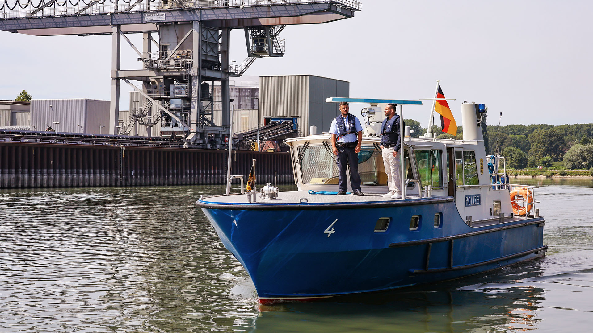 Ein Polizeiboot läuft in den Karlsruher Hafen ein. Im Hintergrund ist ein großer Lastenkran zu sehen.