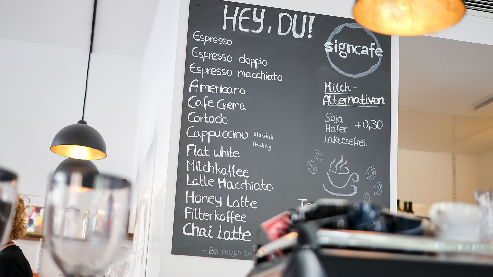Hinter einem Tresen in einem Cafè hängt eine große Tafel mit der Speise- und Getränkekarte.