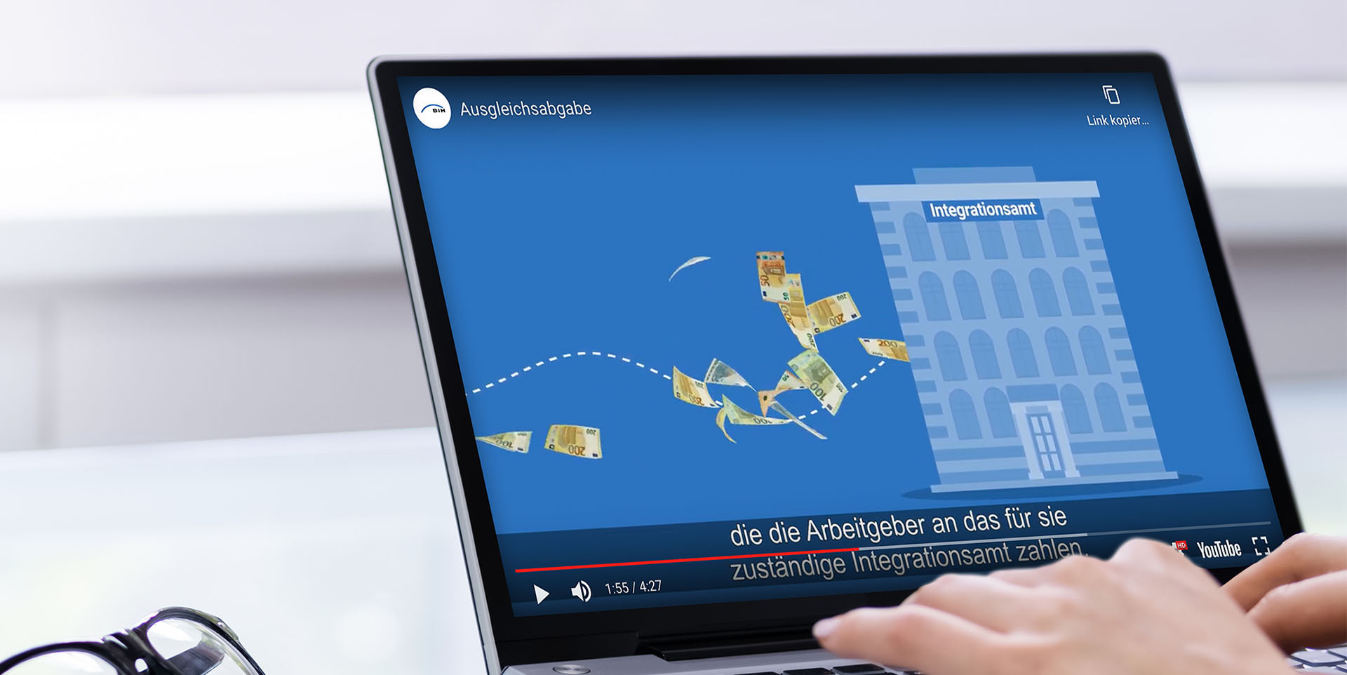 Neue Stufe der Ausgleichsabgabe Auf einem Laptop-Monitor ist ein Ausschnitt eines Erklärfilms zur Ausgleichsabgabe zu sehen. In der Szene fliegen Geldscheine in ein Gebäude, das die Inklusions- und Integrationsämter symbolisiert.