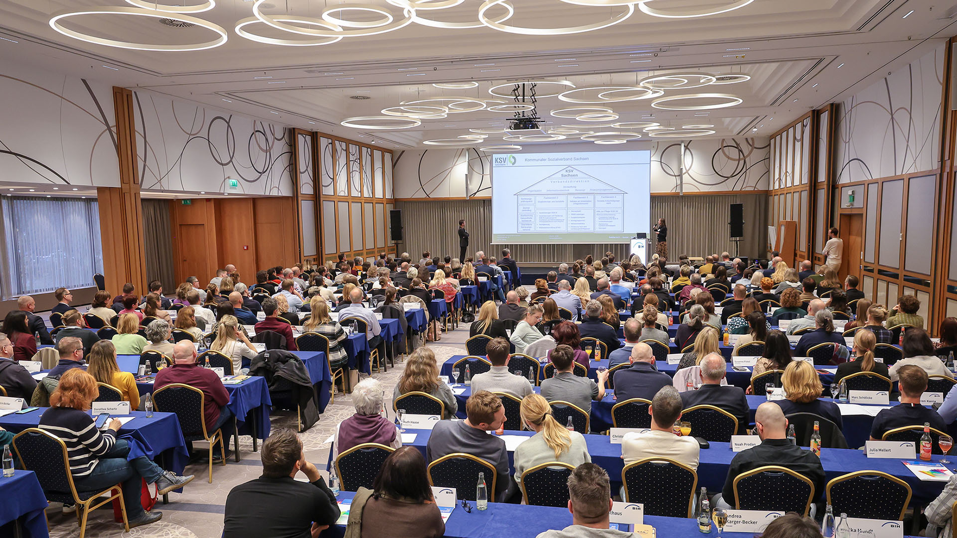 Ein vollbesetzter Saal von hinten zur Bühne hin fotografiert.