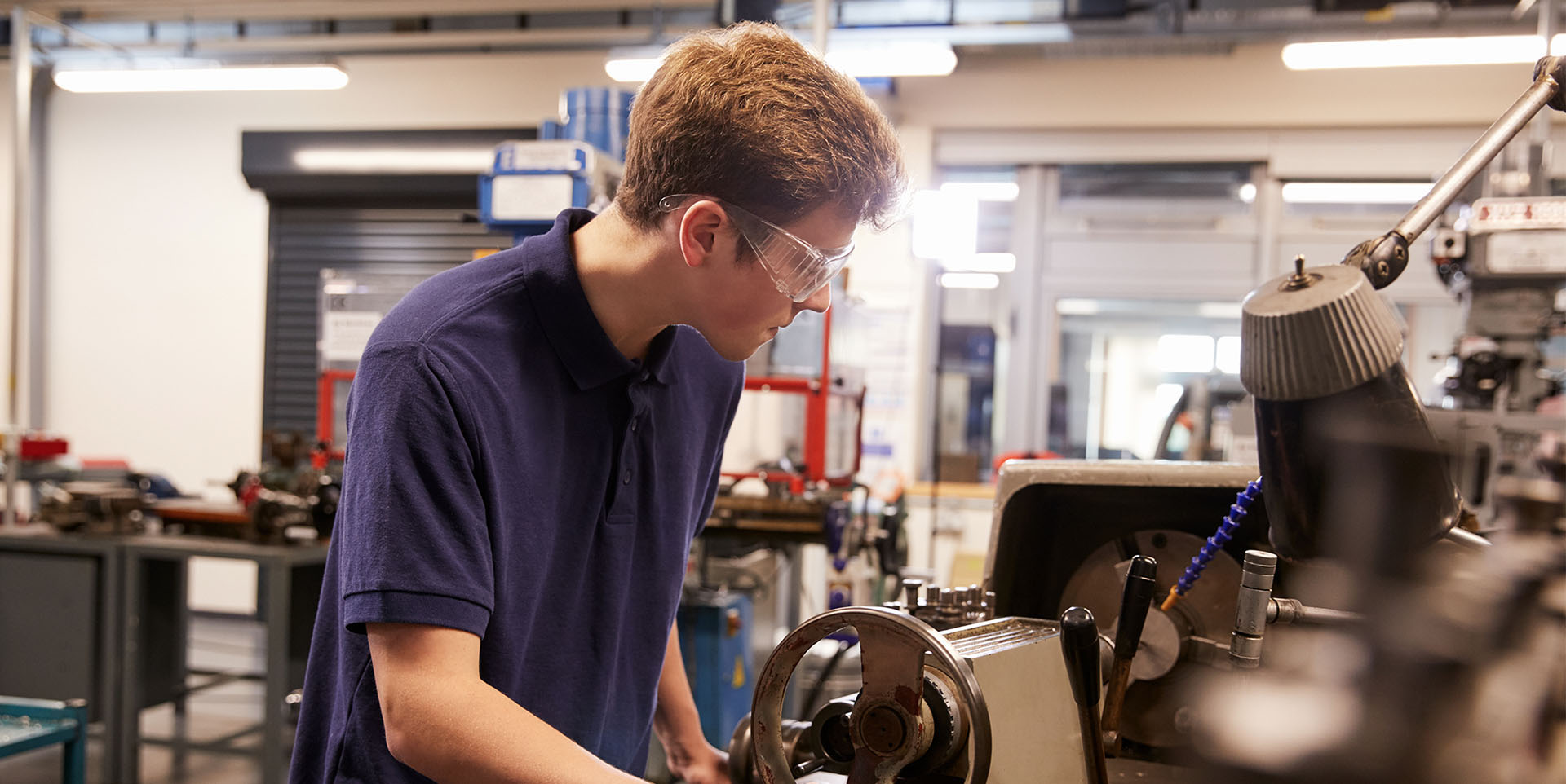 Ausbildung mit ASS Ein junger Azubi steht an einer Drehbank, er trägt eine Schutzbrille.