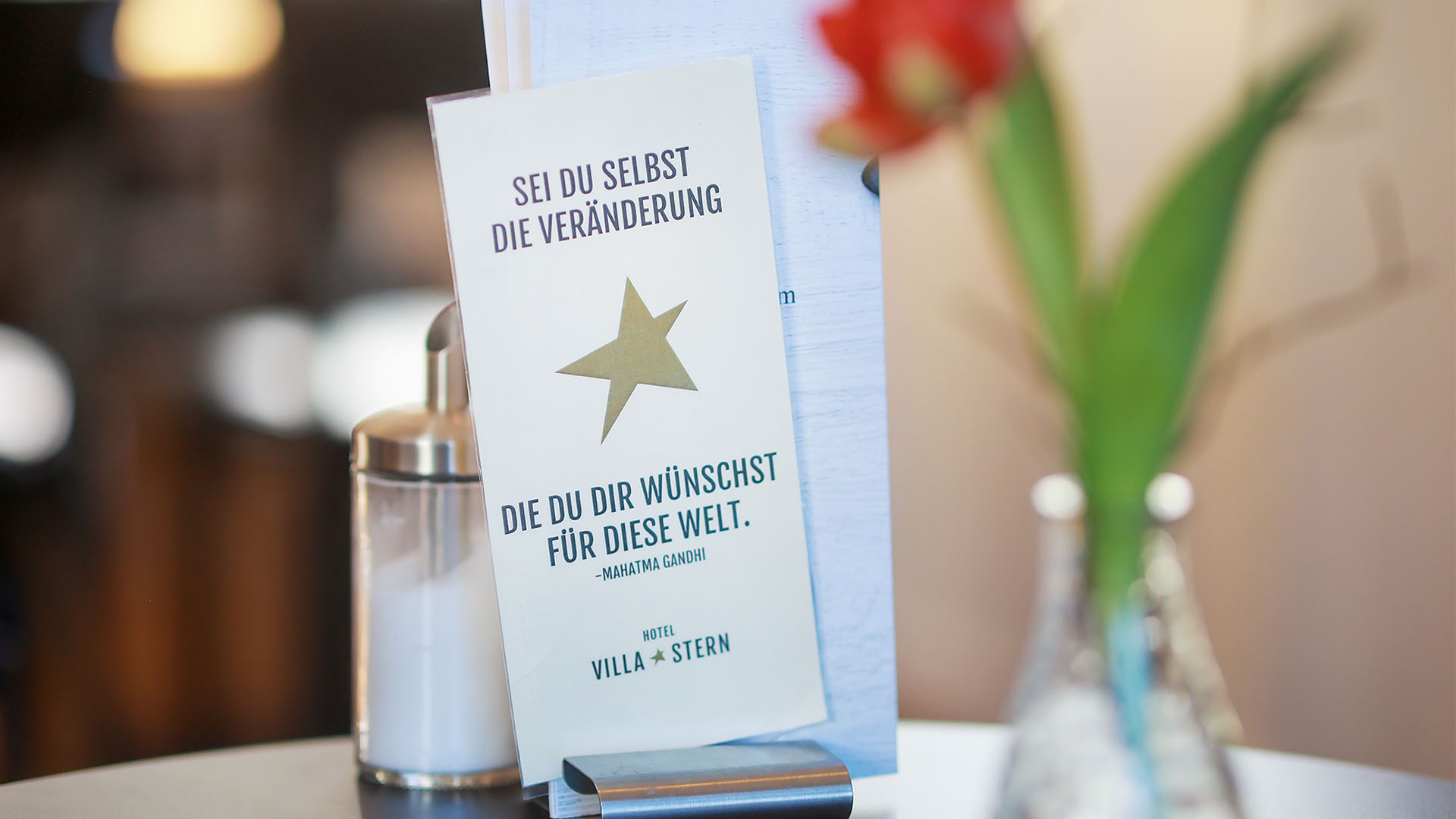 Nahaufnahme der Getränkekarte, die zusammen mit einer roten Blume in einer Vase auf einem Tisch arrangiert ist.
