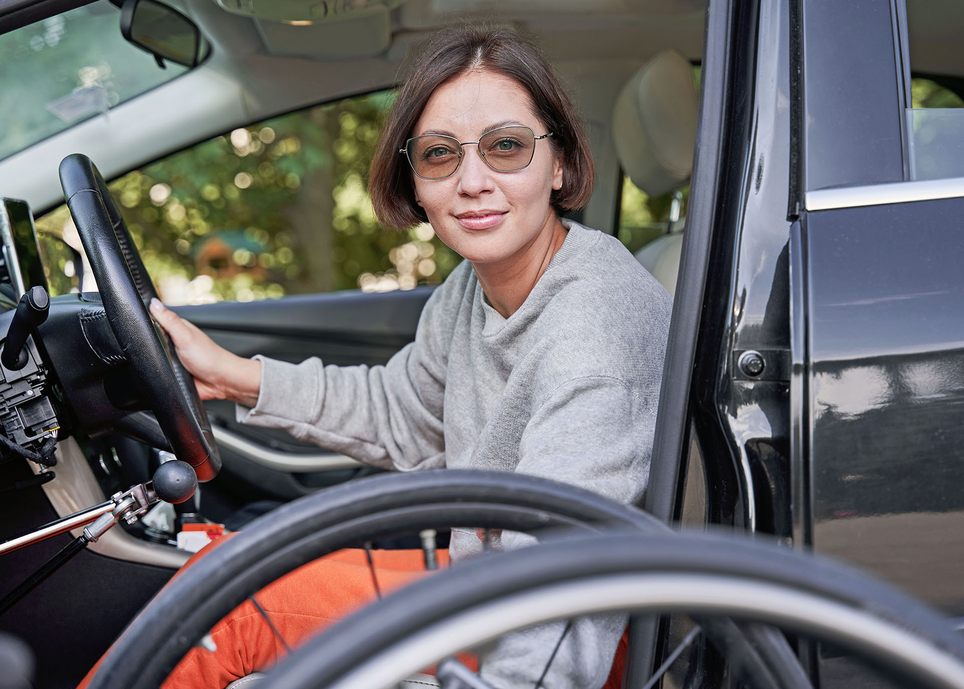 Eine junge Frau sitzt in einem umgebauten Kfz. Ihr Rollstuhl steht neben der geöffneten Fahrertür.