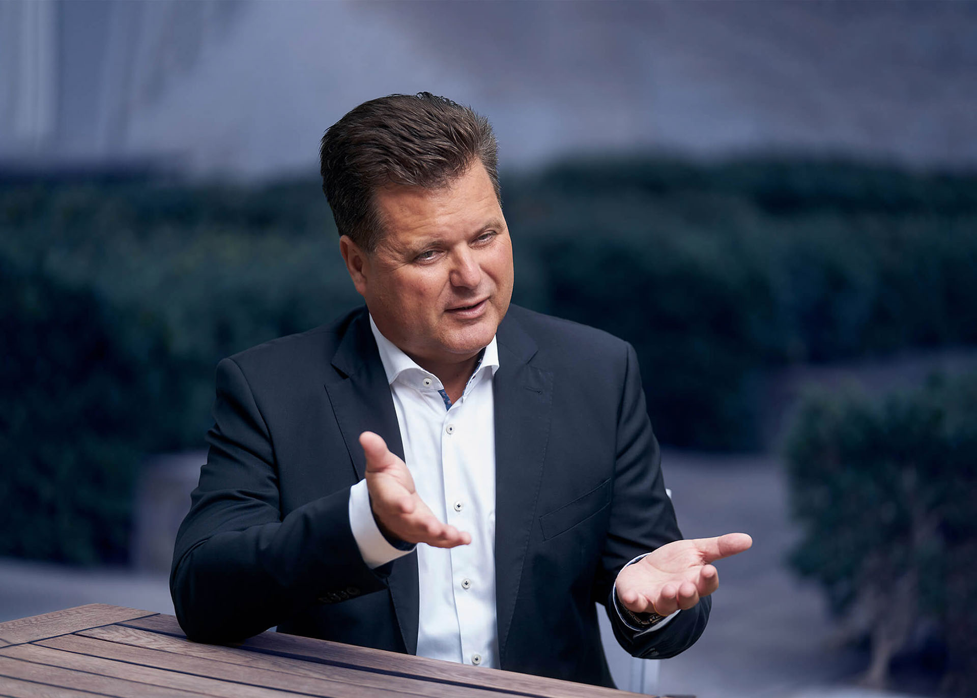 Jürgen Dusel sitzt an einem Tisch. Er trägt ein weißes Hemd und ein dunkelblaues Sakko. Er gestikuliert mit seinen Händen.