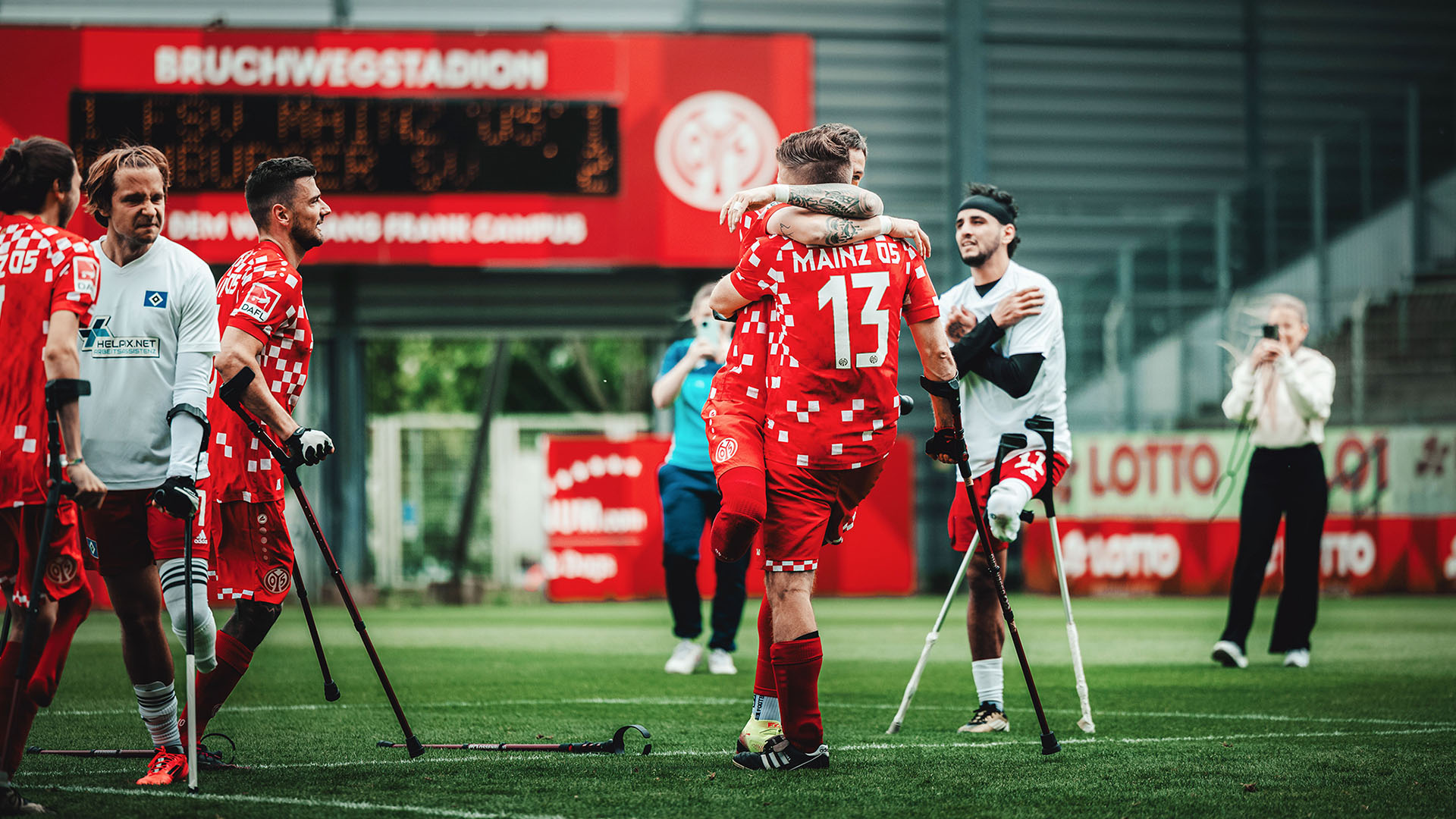 Zwei Amputierten-Fußballer umarmen sich auf dem Feld. Weitere Spieler von beiden Mannschaften stehen drumherum. 