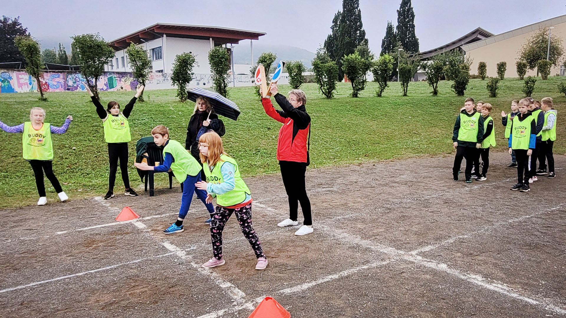 Auf einer Laufbahn sehen zwei Kinder am Start, eine Frau gibt das gerade das Startzeichen. Dahinter stehen weitere Kinder und warten.