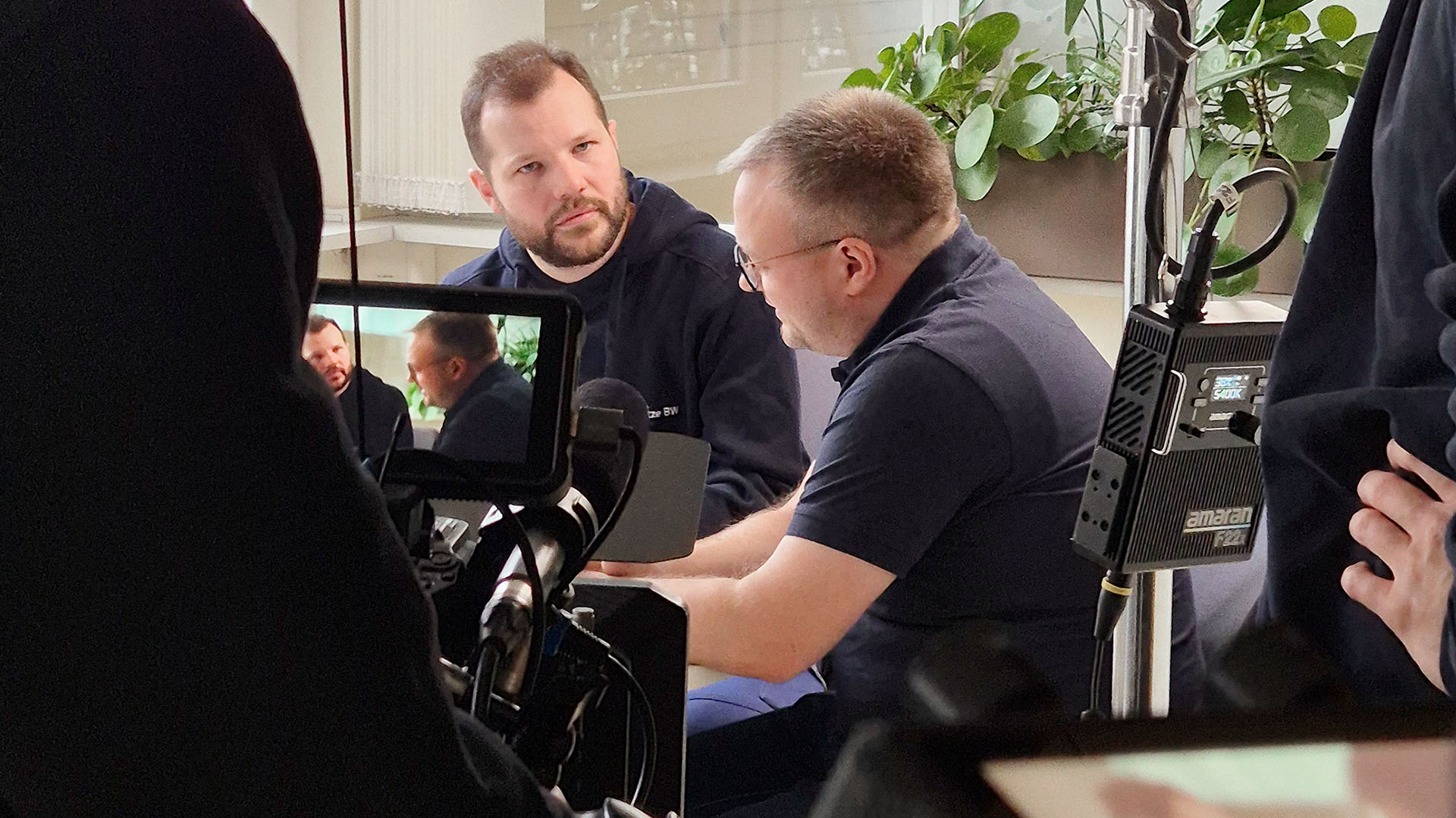 Eine Filmkamera filmt zwei Männer im Gespräch.